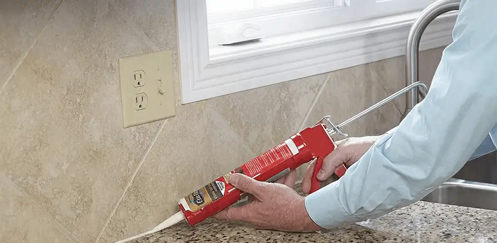 Handyman applying caulk along a kitchen backsplash and countertop seam in Fresno, CA