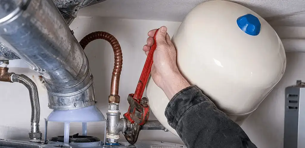 Water heater repair technician tightening plumbing connections near a tank unit in Fresno, CA